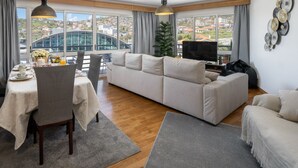 Una sala de estar moderna con sofá, mesa de comedor y sillas. Hay un televisor y una planta en la habitación.