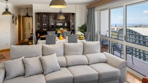 Una sala de estar moderna con un sofá modular, comedor y ventanas amplias con vista a la ciudad.