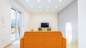 Un salon moderne avec un canapé, un téléviseur posé sur un meuble et une grande fenêtre.