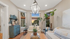 A living room with a wooden floor, a white sofa, a blue cabinet, a glass-top coffee table, and a hanging light fixture. - Perfect 4 Families, Mins 2 Beach, Amazing Backyard (Ventura)