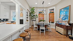 A modern kitchen with white cabinets, a large island with stools, a dining area with a round table and chairs, and a large painting on the wall. - Perfect 4 Families, Mins 2 Beach, Amazing Backyard (Ventura)