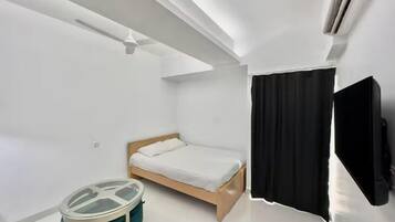 A modern hotel room with a single bed, a small round table, a ceiling fan, and a TV.