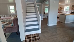 A staircase leading to a second floor, a living room with a sofa and a coffee table, and a kitchen area with a sink and countertop. - Heritage Homeplace in the Highlands (Farmington)