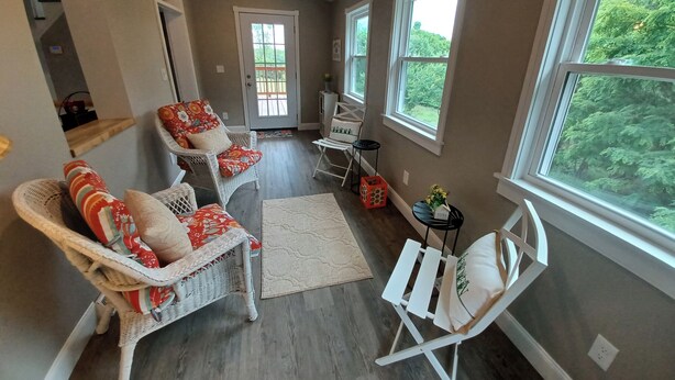 A spacious room with a large window, a door leading outside, and a seating area with wicker furniture and a small table. - Heritage Homeplace in the Highlands (Farmington)