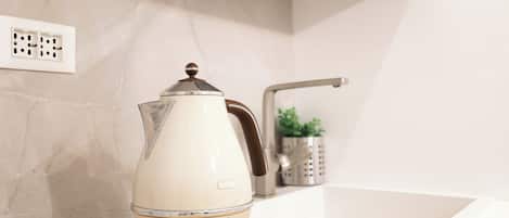 A kitchen with a white countertop, a kettle, and a power outlet on the wall.