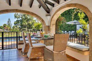 Un coin repas avec des chaises en osier et une table dressée pour deux personnes, donnant sur une piscine et un espace verdoyant.