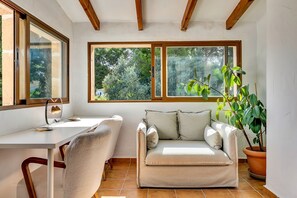 Une pièce confortable avec un bureau, un coin salon agrémenté de coussins, de grandes fenêtres et une plante en pot.