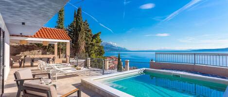A pool area with lounge chairs and a view of the sea.