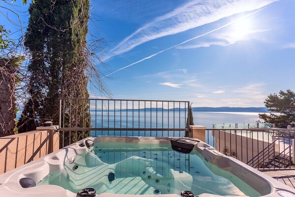A hot tub with a view of the sea and mountains, surrounded by a metal railing and a gate.