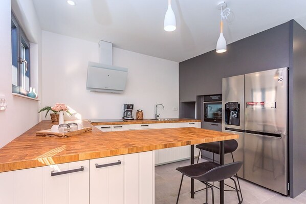 A modern kitchen with a wooden countertop, stainless steel appliances, and a built-in oven. - Villa Tadsi - Four Bedroom Villa, Sleeps 8 (Pisak)