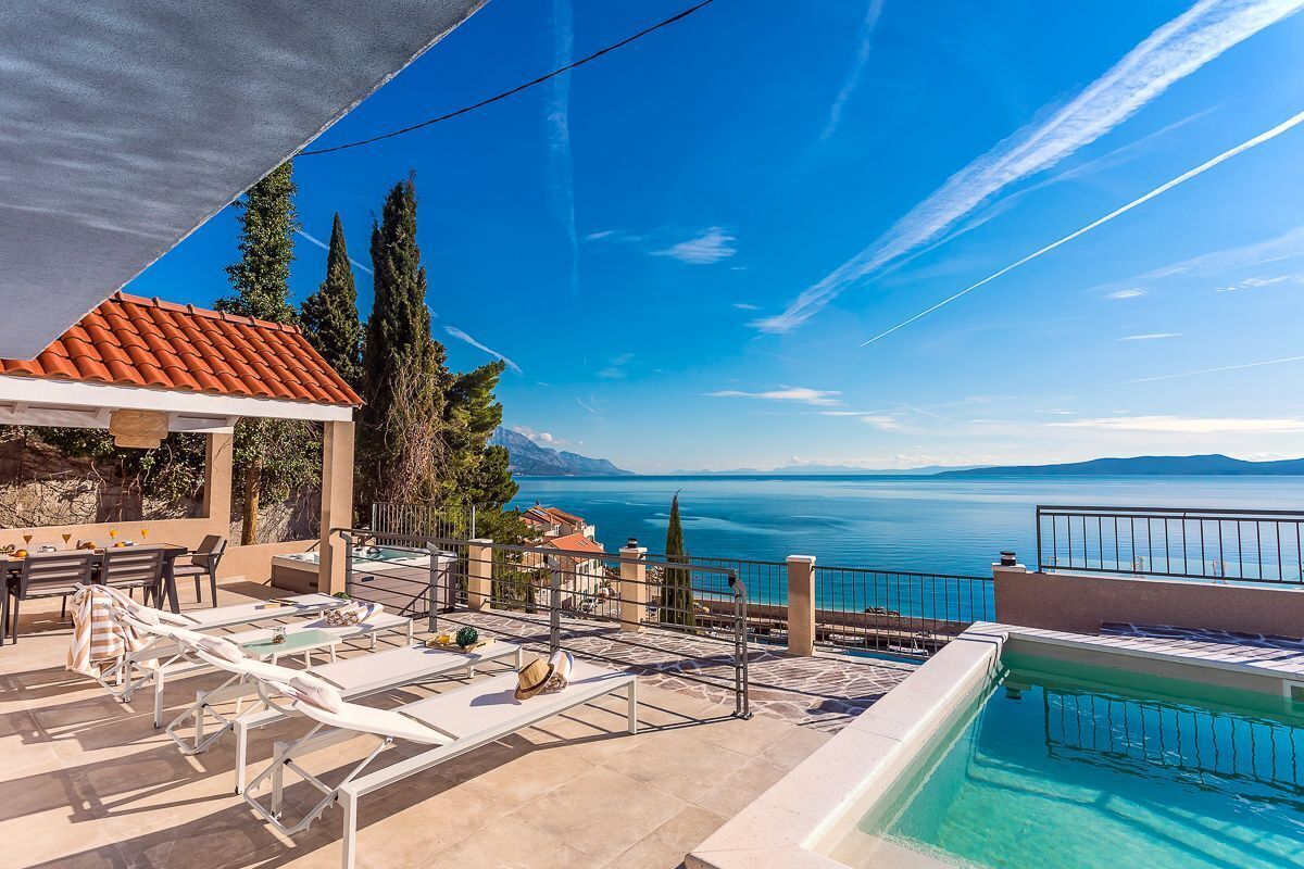 A rooftop pool area with lounge chairs, a small pool, and a scenic view of the sea and mountains.