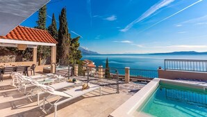 Un espace piscine sur le toit, comprenant des chaises longues, une petite piscine et une vue panoramique sur la mer et les montagnes.