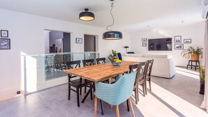 Et moderne spiseområde med et træbord, sorte stole og en blå stol med hynde. Der er en skål med frugt på bordet, og en loftlampe hænger over.