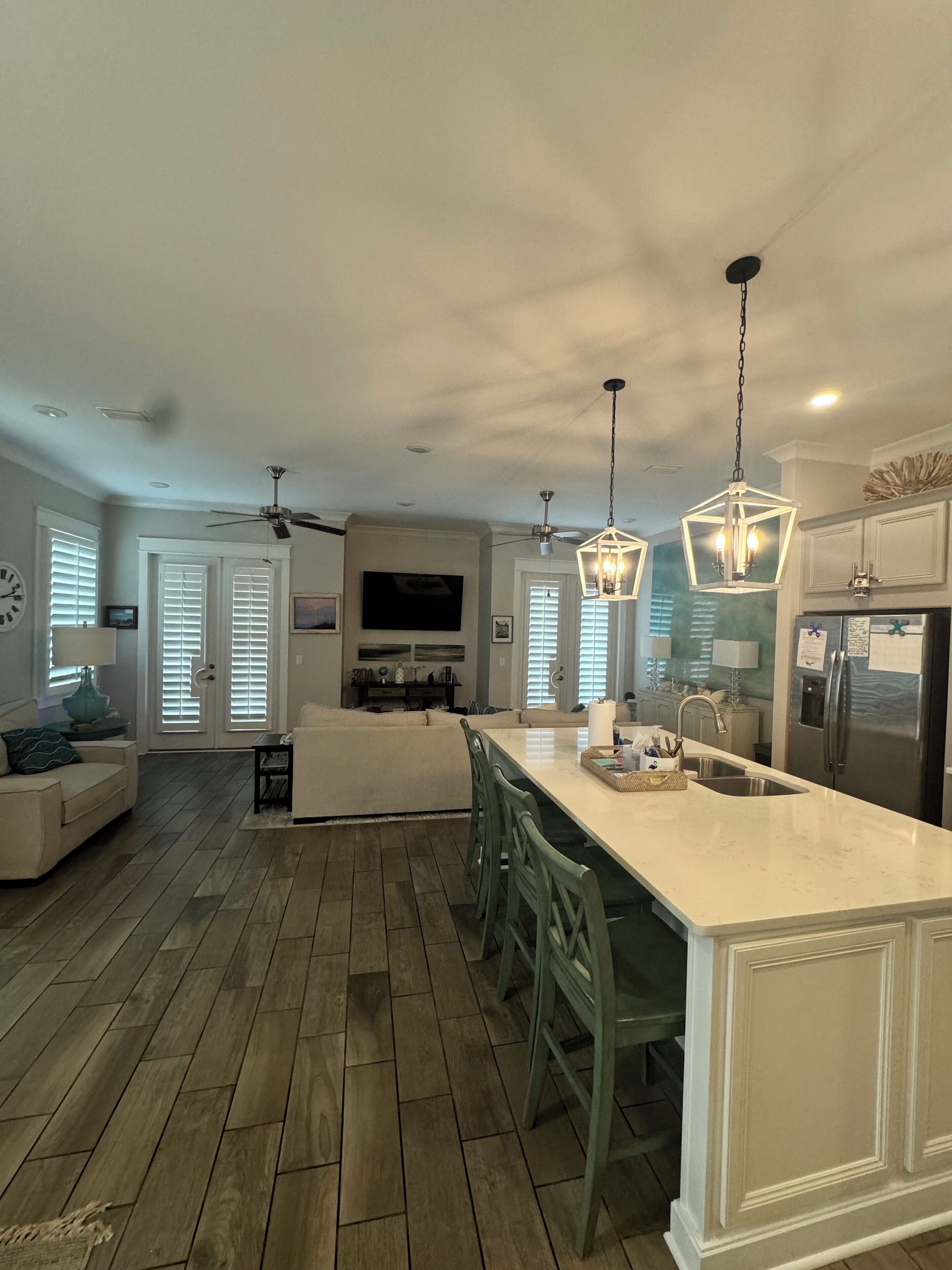 A modern kitchen with a large island, wooden flooring, and pendant lighting.