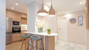 A modern kitchen with a central island, bar stools, and pendant lighting. - Genteel Home Fuente Nueva (Granada)