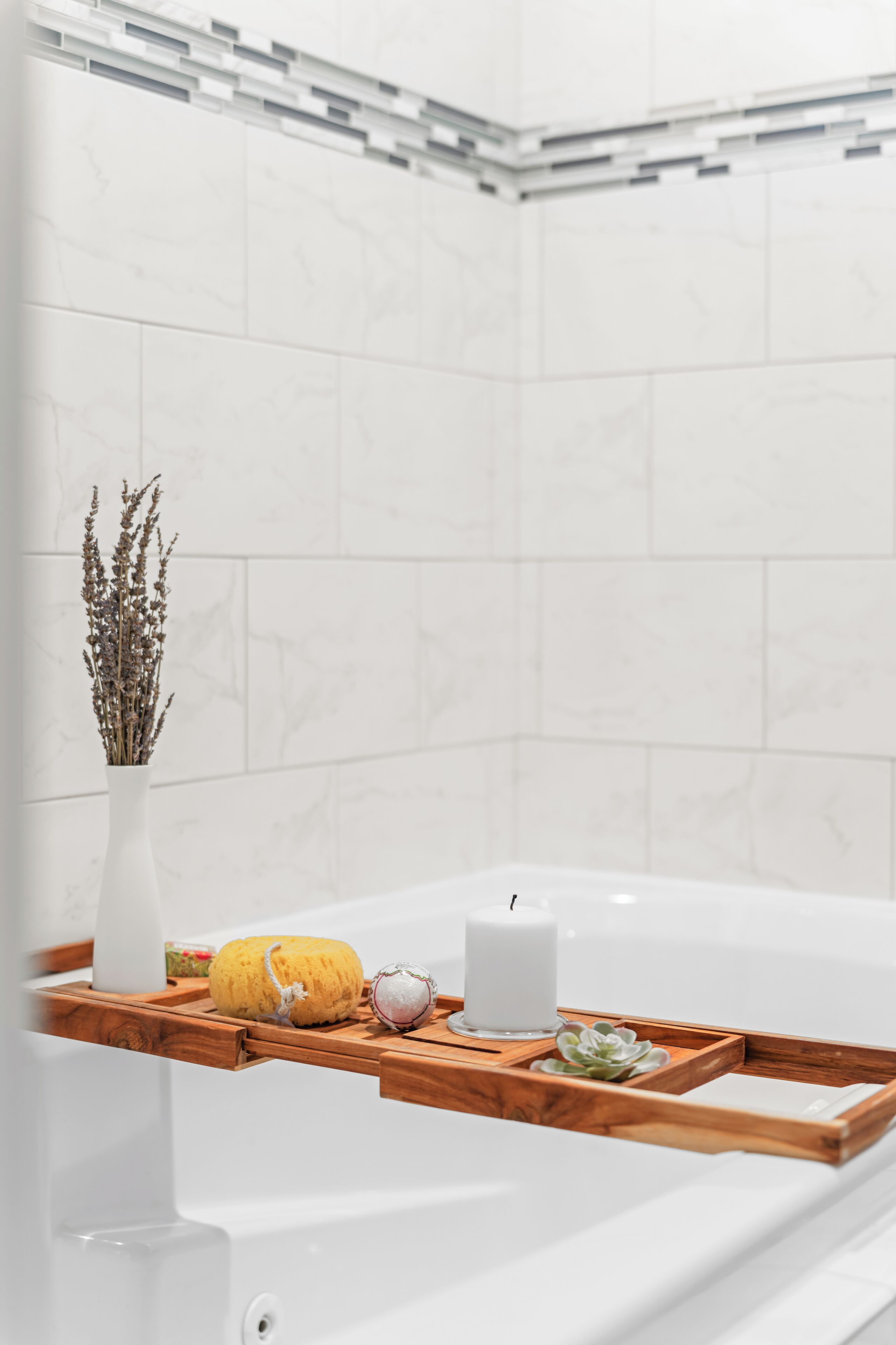 Um banheiro com uma banheira branca, uma prateleira de madeira com um vaso de flores secas, uma abóbora e uma vela.