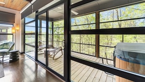Una stanza spaziosa con ampie finestre, un terrazzo in legno e vista sugli alberi.