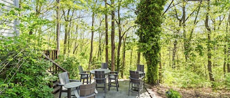 An outdoor patio with stone flooring and wooden furniture, surrounded by trees and greenery.