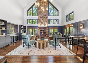 A spacious living room with a stone fireplace, large windows, and a high ceiling. - Iris Inn and Cabins (Waynesboro)