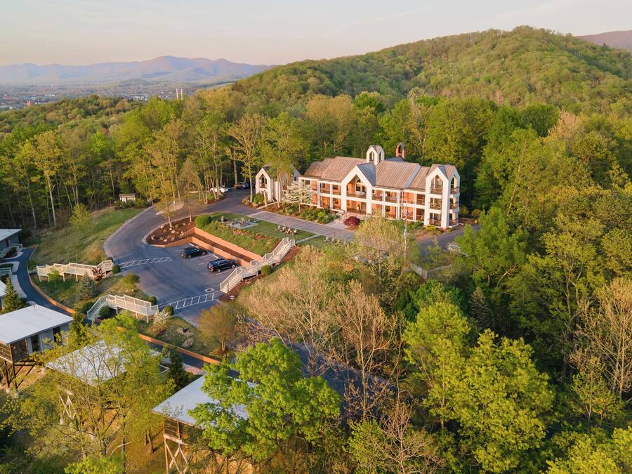 A large, multi-story building surrounded by dense forest, with a spacious driveway and a small parking area.