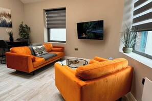 Een moderne woonkamer met oranje banken, een salontafel en een aan de muur bevestigde televisie.