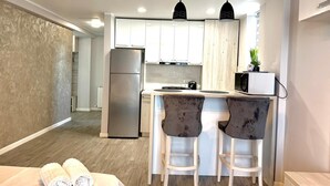 A modern kitchen with white cabinets, a stainless steel refrigerator, two bar stools, and pendant lighting.