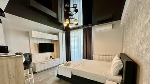 A modern hotel room with a bed, a desk, a TV, and a unique geometric light fixture.