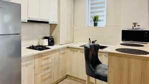 A modern kitchen with white cabinets, a stainless steel refrigerator, a black microwave, and a black chair.