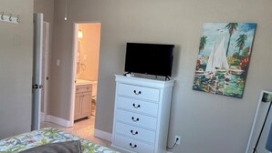 Une chambre à coucher avec un lit, une commode, un téléviseur et un tableau.
