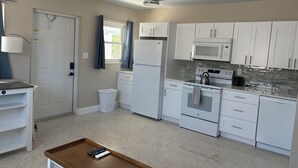 Une cuisine compacte avec des meubles blancs, un four à micro-ondes, une cuisinière et une poubelle.
