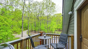 A wooden deck with two chairs and a small table, overlooking a forested area.
