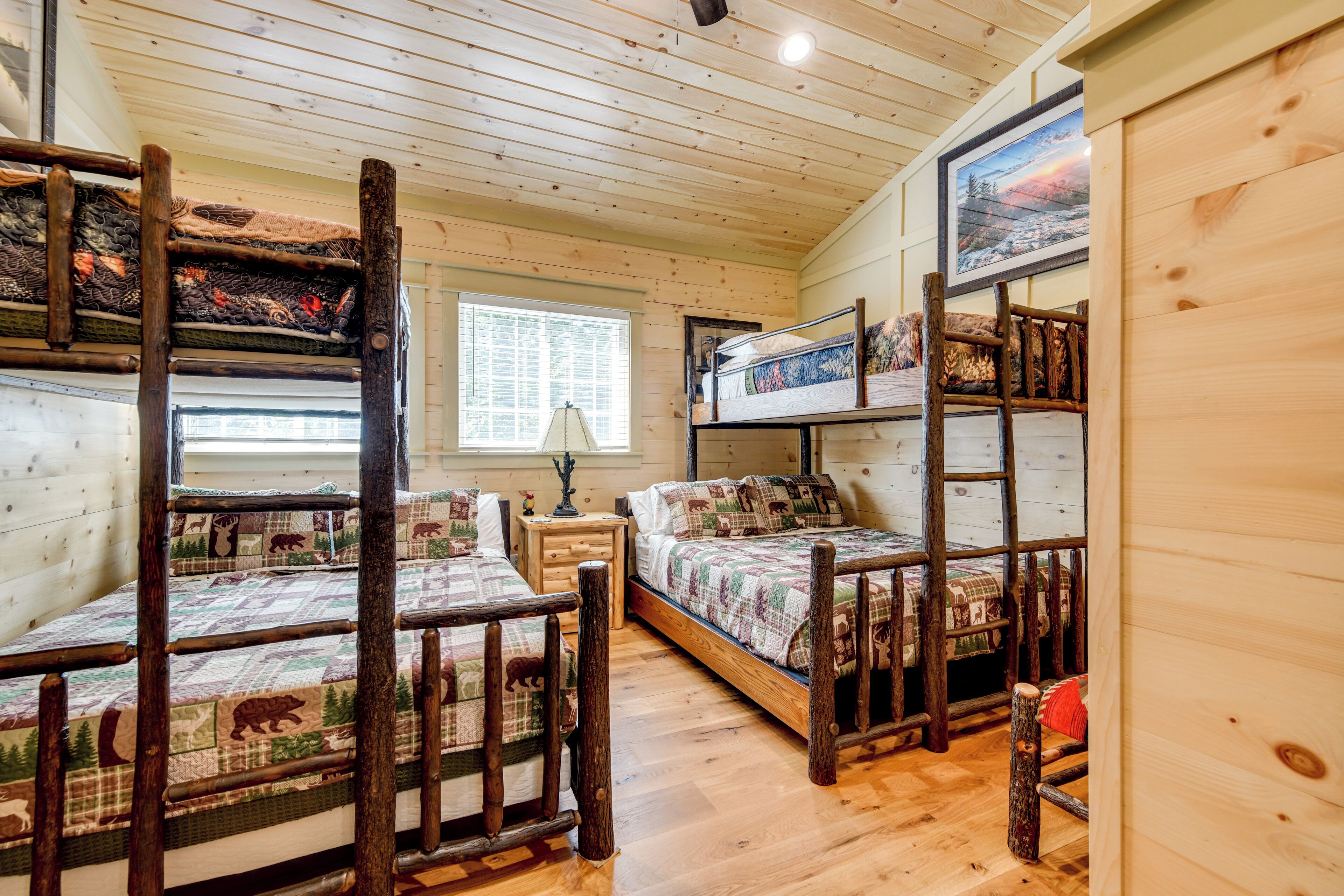 A cabin with bunk beds, wooden floors, a window with blinds, and a framed picture on the wall.