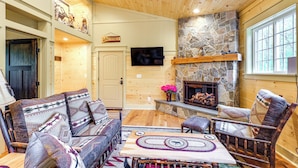 A cozy living room with a stone fireplace, wooden furniture, and a television mounted on the wall.