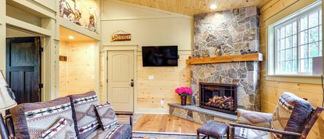 Una sala de estar acogedora con chimenea de piedra, muebles de madera y un televisor montado en la pared.
