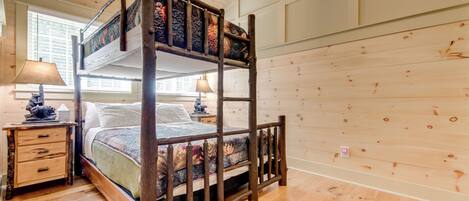 A bunk bed with a wooden frame and a patterned mattress, a bedside table with a lamp, and a window with blinds.