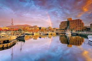 A marina with boats docked, a large building with a grid-like facade, and a mountain in the background.
