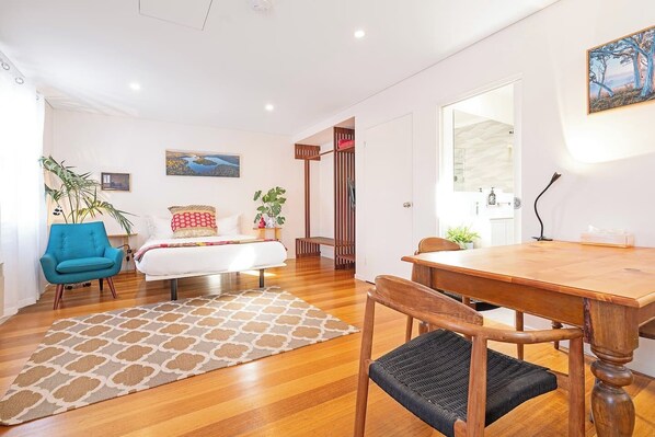 Un dormitorio moderno con cama, un sillón azul, una mesa de comedor de madera y un ventanal grande.