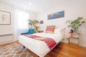 Una habitación de hotel con una cama grande, una silla azul, una planta en maceta y un cuadro en la pared.