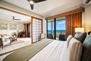A hotel room with a bed, a seating area with a sofa and chairs, a television, and a view of the ocean.