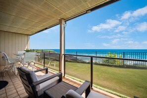 A covered outdoor area with a table and chairs, a view of the ocean, and a grassy lawn.