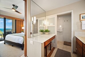 A hotel room with a bed, a bathroom with a shower, a mirror, and a view of the outside.