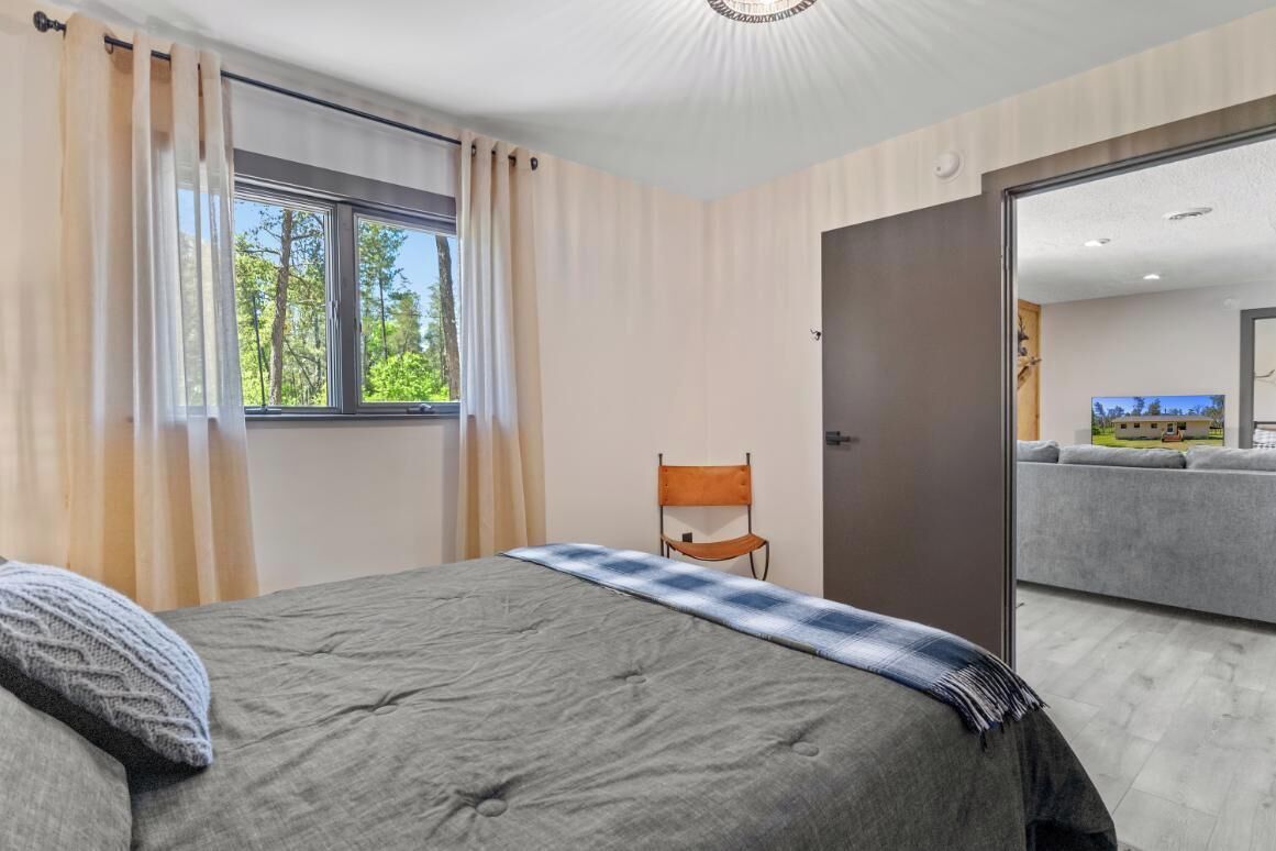 A bedroom with a bed, a chair, a window, and an open door leading to a living area.