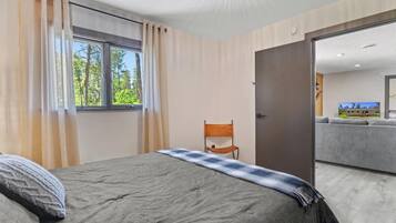 A bedroom with a bed, a chair, a window, and an open door leading to a living area.