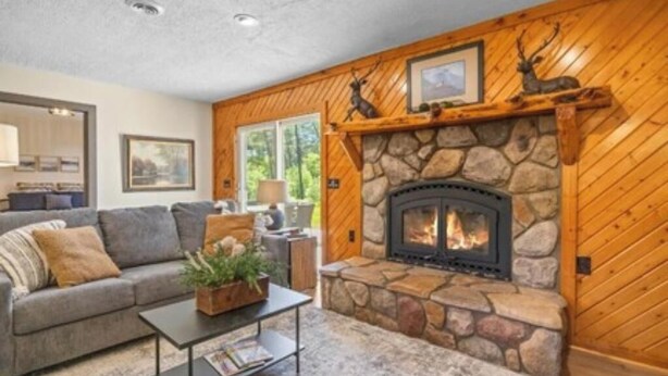 A cozy living room with a stone fireplace, wooden walls, a sofa, and a coffee table. - Cozy Lodge on 10 acres- Sleeps 9, Newly Renovated, Game Room, Lg Deck, Irons MI. (Irons)