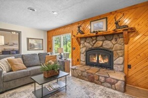 Una sala de estar acogedora con chimenea de piedra, paredes de madera, un sofá y una mesa de centro.