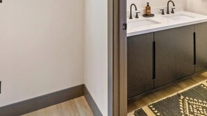 A modern bathroom with a double sink, vanity, and a ceiling light fixture. - Cozy Lodge on 10 acres- Sleeps 9, Newly Renovated, Game Room, Lg Deck, Irons MI. (Irons)