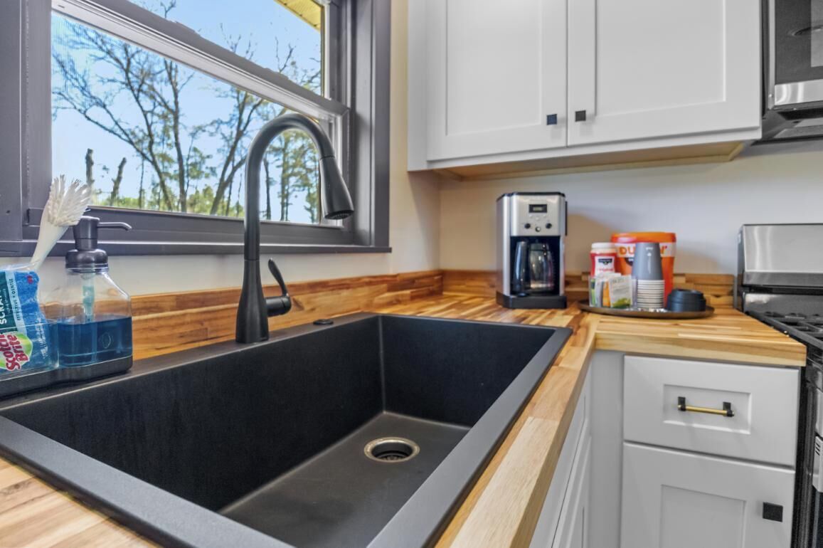A kitchen with a black sink, a window, wooden countertop, and white cabinets.