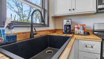 A kitchen with a black sink, a window, wooden countertop, and white cabinets.