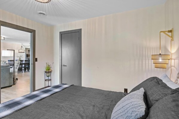 Un dormitorio con una cama, una puerta, una lámpara de pared y vistas a otra habitación.