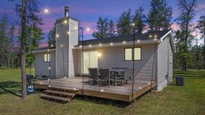 A modern cabin with a deck, a chimney, and string lights. - Cozy Lodge on 10 acres- Sleeps 9, Newly Renovated, Game Room, Lg Deck, Irons MI. (Irons)